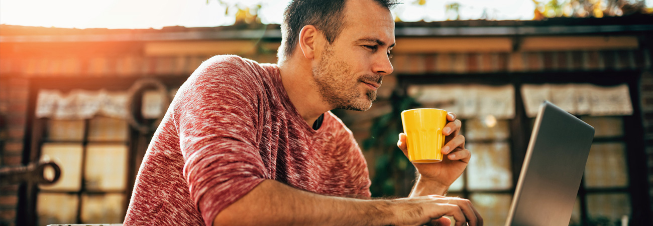 Mann sitzt mit Kaffeetasse vor Laptop