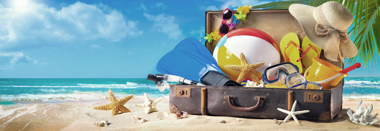 Ein Koffer voller Stranduntensulien steht am Strand vor Meereskulisse.