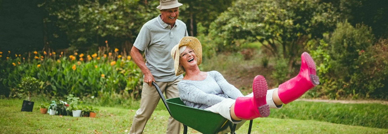 Senior fährt seine lachende Frau in der Schubkarre spazieren