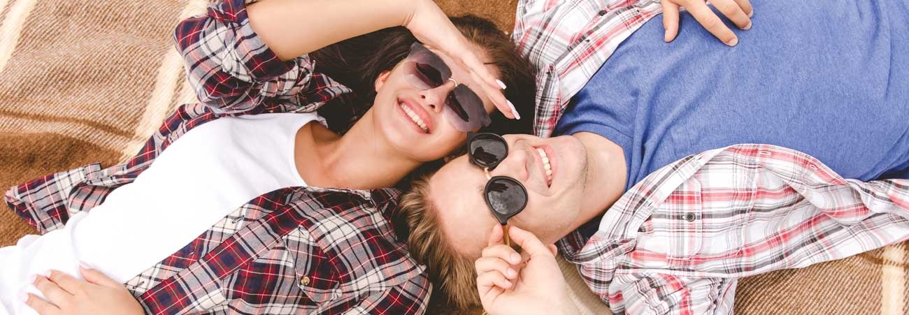 Junges Paar liegt entspannt auf einer Decke im Freien und lächelt in die Sonne
