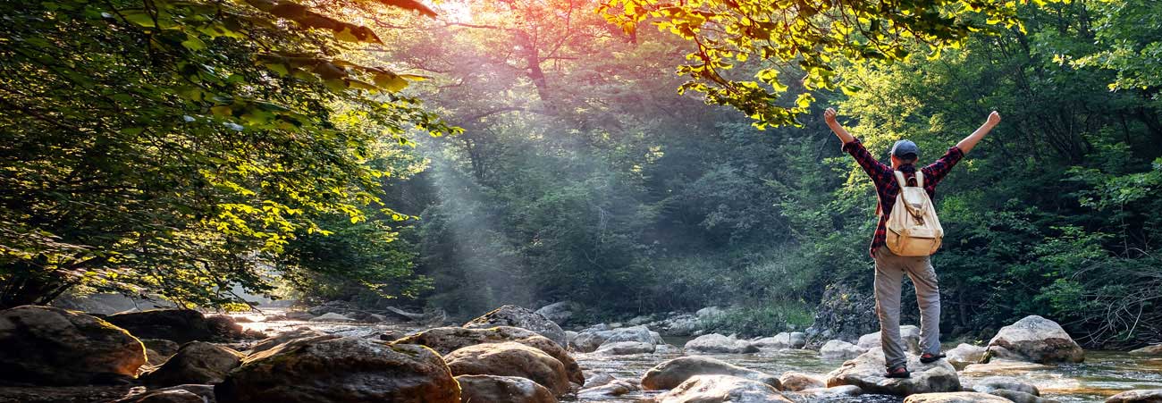 Wanderer steht auf Steinen im Fluss und genießt die Natur.