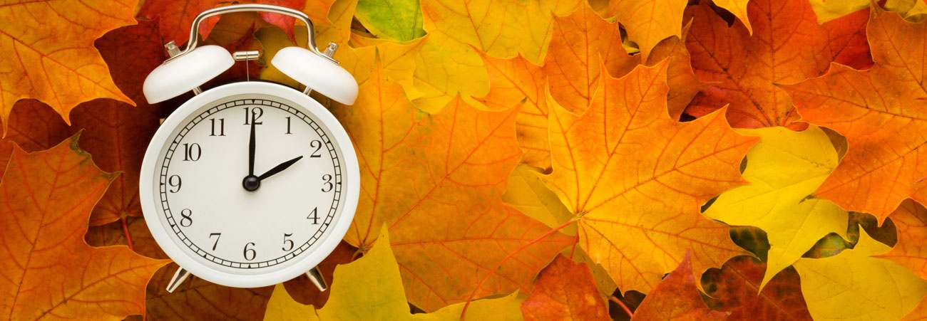 Ein Wecker zeigt 2 Uhr an und liegt auf buntem Herbstlauf.