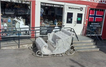 Weißer nostalgischer Schlitten, der aussieht wie vom Weihnachtsmann,  steht vor dem Eingang eines Geschäfts in Norwegen - nordisches Weihnachtsambiente abseits der Legende