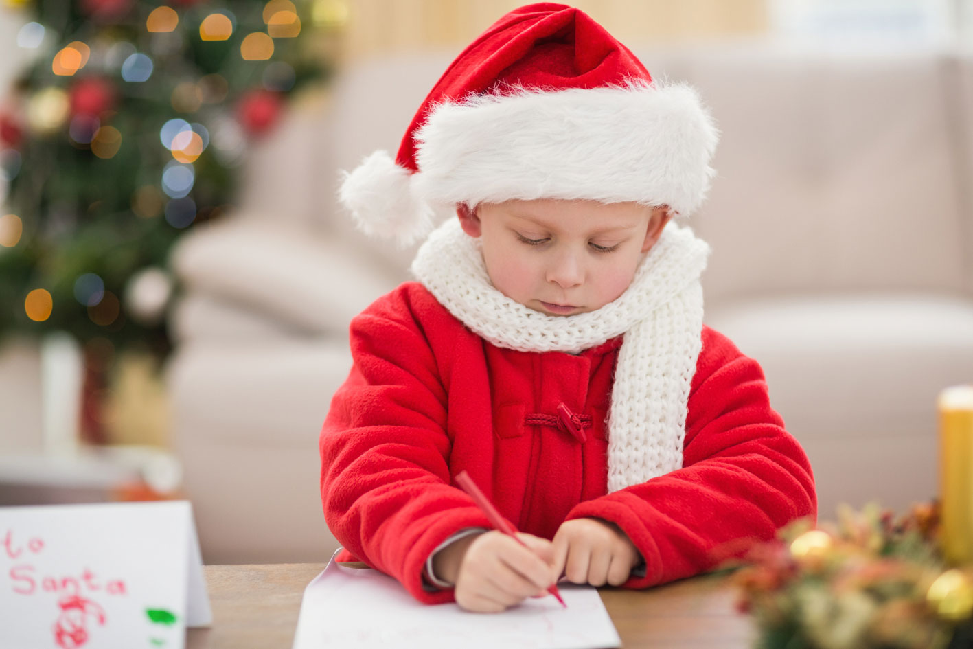 Kleiner Junge im roten Weihnachtsmantel malt Wunschzettel.