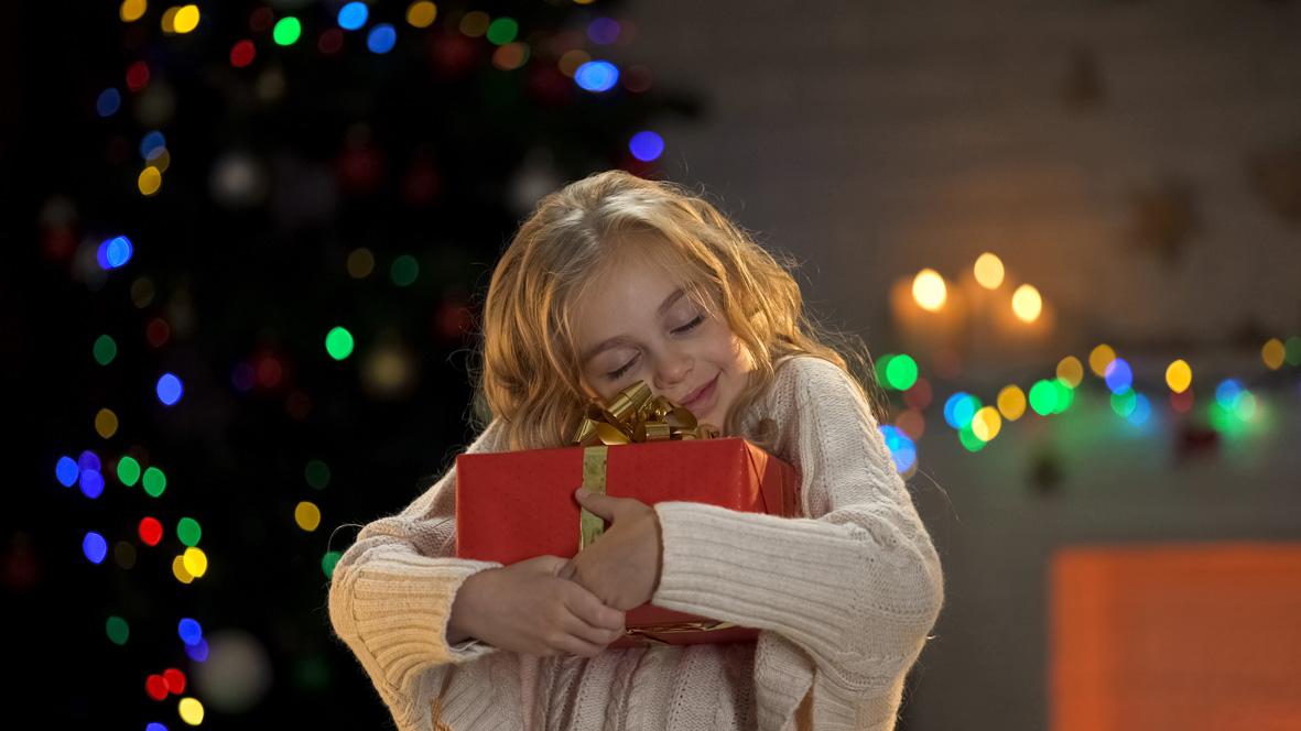 Kleines Mädchen umarmt innig ein Geschenk.