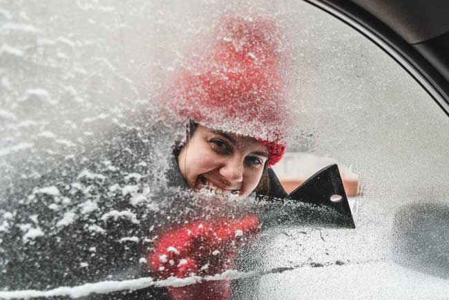 junge Frau kratzt Autoscheibe frei