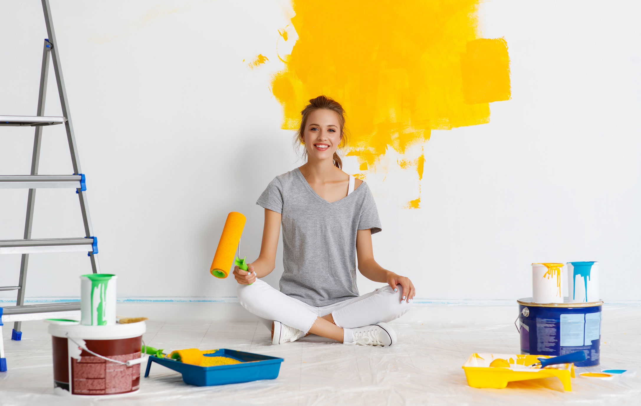 Junge Frau sitzt mit Malerbuerste vor gelb gestrichener Wand