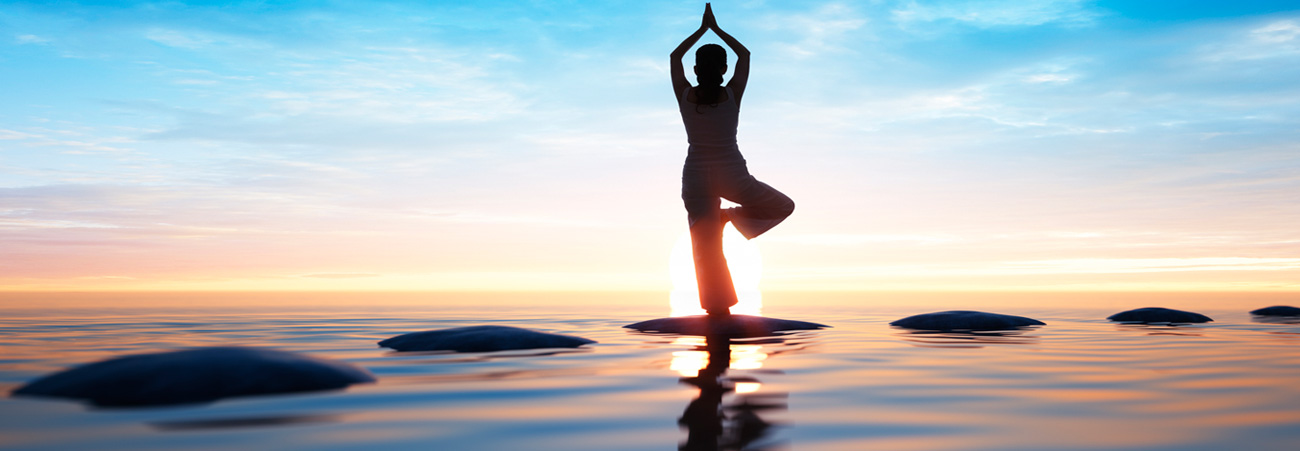 Frau steht bei Sonnenaufgang im Yoga-Einbeinstand am Meer.