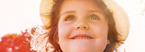 Kleines Mädchen mit Sonnenhut blickt lächelnd in die Ferne. 