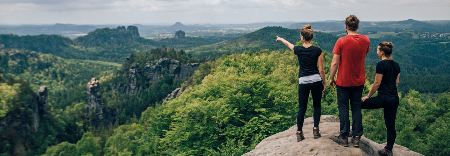 Drei junge Menschen schauen von einem Felsen ins Land.