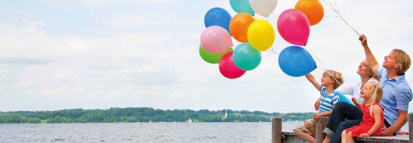 Familie mit bunten Luftballons auf einem Steg am Wasser sitzend
