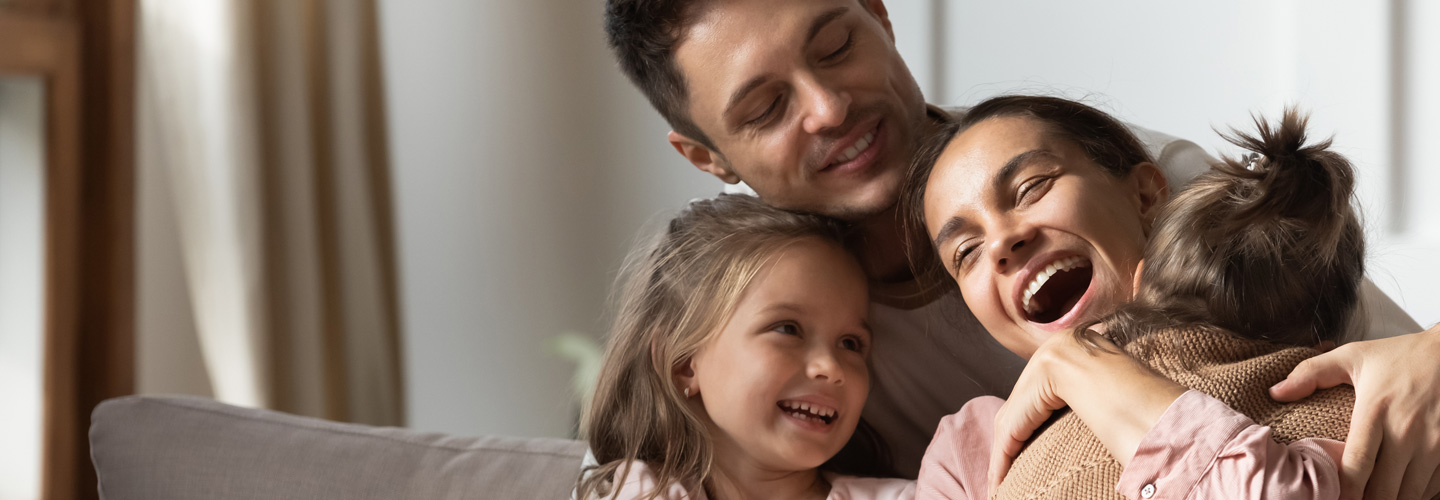 Familie lacht und kuschelt auf dem Sofa.