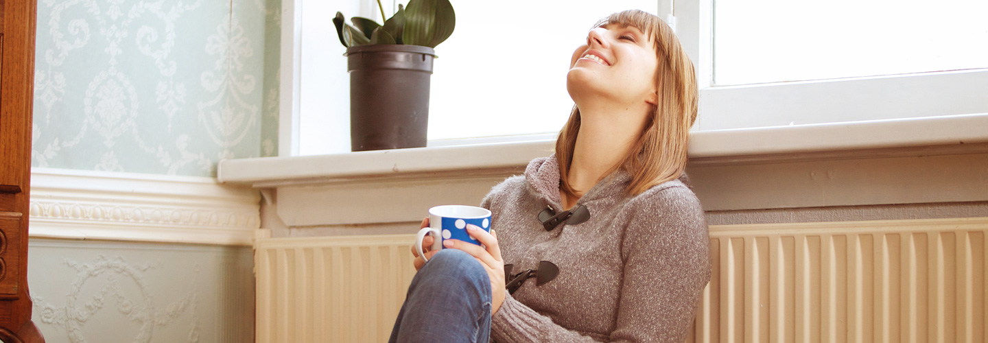 Frau sitz mit einem Tee auf dem Boden und lächelt. 