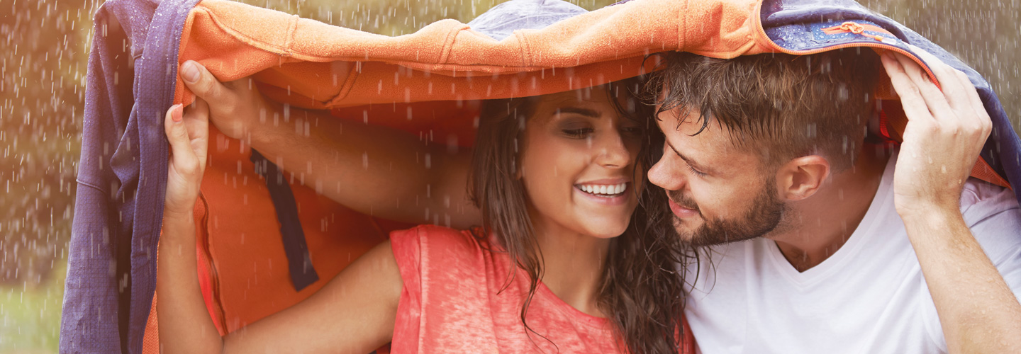 Junges Paar unter einer Jacke im Regen.