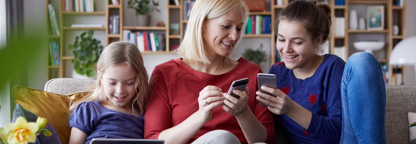 Frau spielt mit ihren zwei Töchtern am Smartphone.